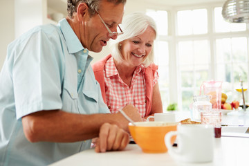Middle Aged Couple Looking At Digital Tablet Over Breakfast