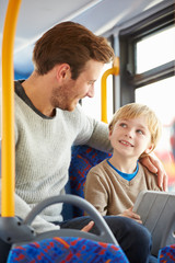 Son Using Digital Tablet On Bus Journey With Father