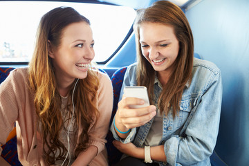 Two Young Women Reading Text Message On Bus