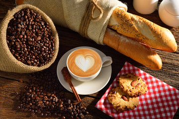 A cup of cafe latte with coffee beans and bread.