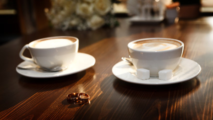 Two cups of coffee on the table, with wedding rings.
