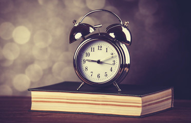 Alarm clock and book. Photo in old color image style.