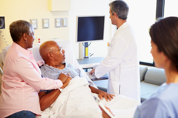 Medical Team Meeting With Senior Couple In Hospital Room