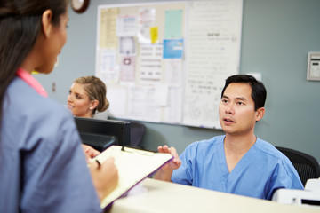 Male And Female Nurse In Discussion At Nurses Station
