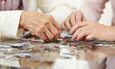 Fototapeta na wymiar Old hands solving jigsaw puzzle