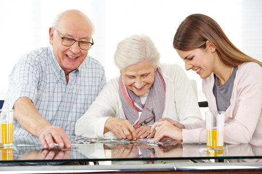 Social worker solving jigsaw puzzle with senior couple