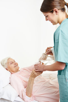 Geriatric nurse giving water to senior woman