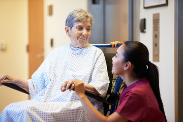 Senior Female Patient Being Pushed In Wheelchair By Nurse - obrazy, fototapety, plakaty