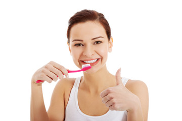 Beautiful woman in white top is brushing her teeth.