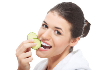 Beautiful woman in bathrobe holding slices of cucumber.