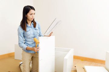 Asian woman assembling furniture with instruction