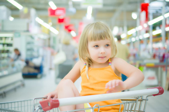 Adorable girl at shopping cart grimacing in supermarket