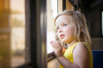 Adorable girl ride by bus and look through open window outside