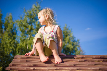 Adorable girl sit on kids house roof on playground