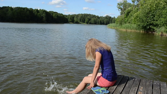 girl sitting on bridge large lake slosh water feet sunny day
