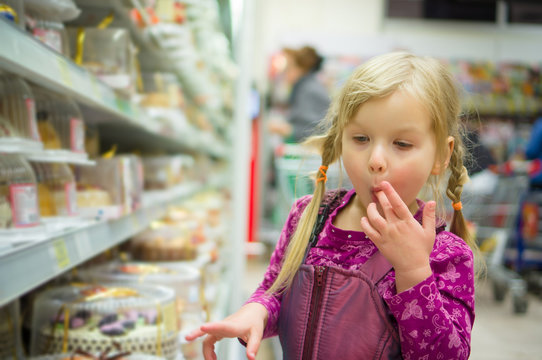 Adorable girl at shopping cart select sweet cakes in supermarket