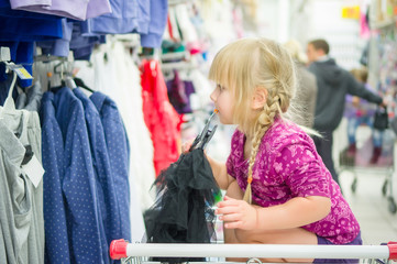 Adorable girl on shoppping cart select clothes in supermarket