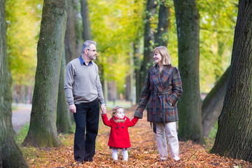 Naklejka na ściany i meble Happy couple walking in an autumn park with a toddler girl