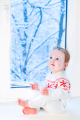 Sweet little baby sitting at a window watching the snowy garden