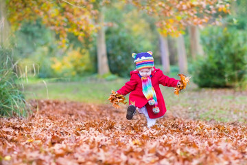 Baby girl wearing a red coat and colorful knitted hat in leaves