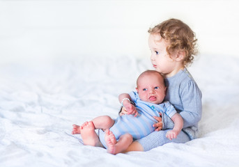 Adorable toddler girl holding her newborn baby brother