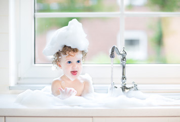 Cute happy baby girl with big blue eyes playing with water in a