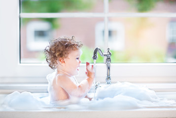 Funny happy baby girl playing in a kitchen sink full with foam