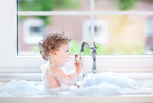 Funny Happy Baby Girl Playing In A Kitchen Sink Full With Foam