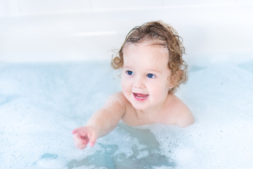 Fototapeta na wymiar Smiling baby girl with beautiful blue eyes playing with foam