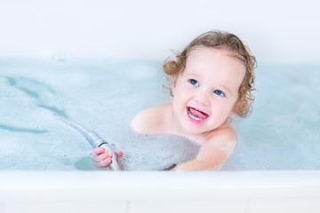 Beautiful little baby girl with big blue eyes playing in a bath