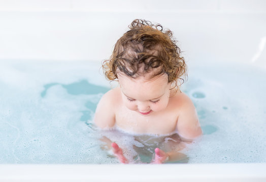 Baby girl with curly hair playing with soap foam in a bath