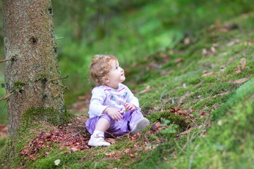 Cute curly baby girl playing in a beautiful pine wood forest in