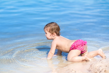 Fototapeta na wymiar Cute little baby crawling on a beach with clear blue water