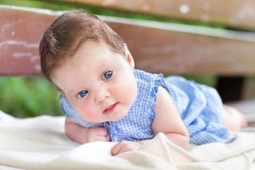 Little baby girl relaxing on her tummy on a garden bench