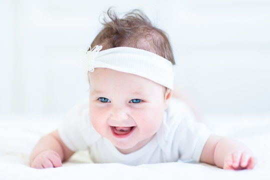 Cute laughing baby girl with a white bow playing on her tummy