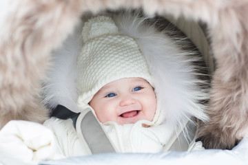Laughing baby girl in a warm stroller wearing a winter jaket