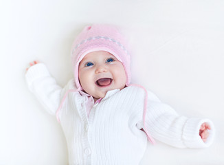 Laughing baby girl in a white knitted sweater and a warm hat