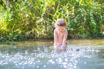 Curly baby girl splashing in a river on a sunny warm day