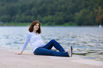 Fototapeta na wymiar Young beautiful pregnant woman relaxing at a river shore