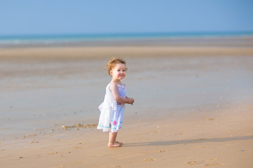 Cute curly baby girl playing on a beautiful tropical beach weari