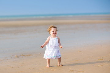 Fototapeta na wymiar Baby girl with curly hair dressed in a white dress in a beach