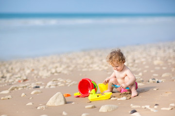 Cute curly baby girl playing with sand on a beautiful beach