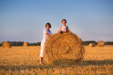 Naklejka na ściany i meble Brother and baby sister in a field of hay bales at sunset