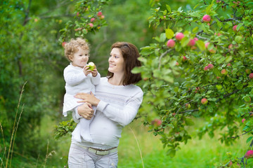 Young pregnant woman and her baby daughter under appletree