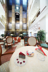 Cup of coffee and piece of cake on table in hall on big hotel.