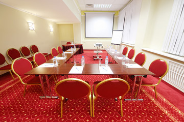 Projector, red chairs and tables with bottles in small room