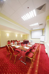 Projector, red chairs and tables with bottles in small room