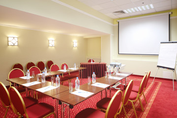 Projector, red chairs and tables in room with red carpet