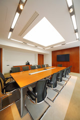 Long wooden table, black armchairs and tv in light room