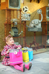 Little girl in pink sits on floor with bags near showcase